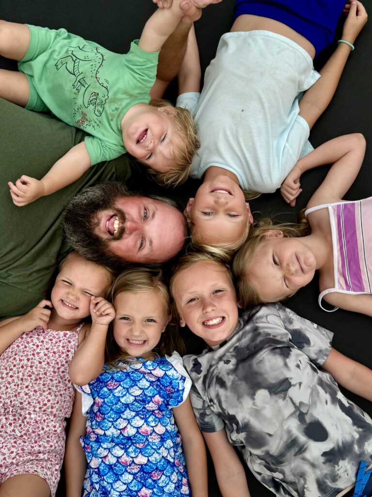 IMG_7685 6 happy kids and dad laying in a cirlce with their heads touching.